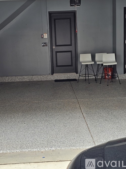 Two white chairs are placed on a grey floor outside a door.