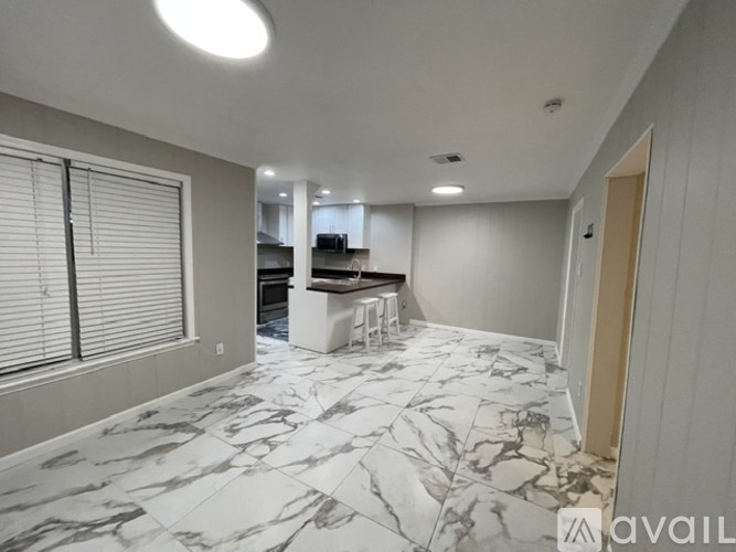 A spacious room with marble flooring and a kitchen area in the background.