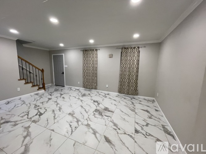 A spacious room with marble flooring and a staircase on the left side.