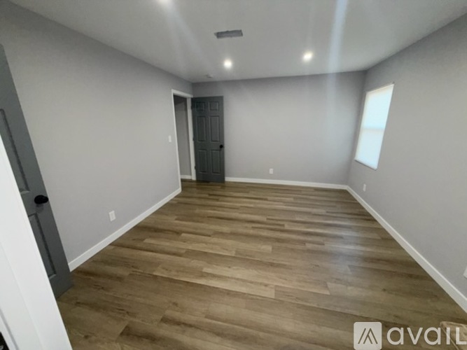 A room with wooden flooring and a door leading to another room.