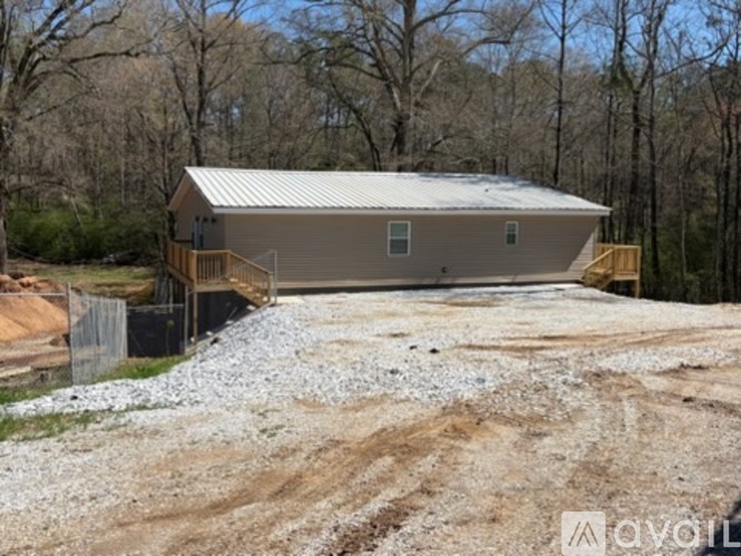 A house with a metal roof is surrounded by a gravel area and trees.