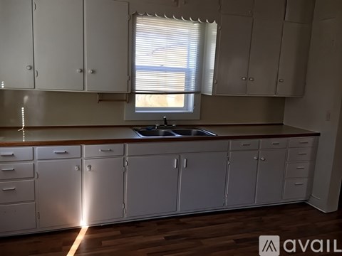 A kitchen with white cabinets and a window with blinds.