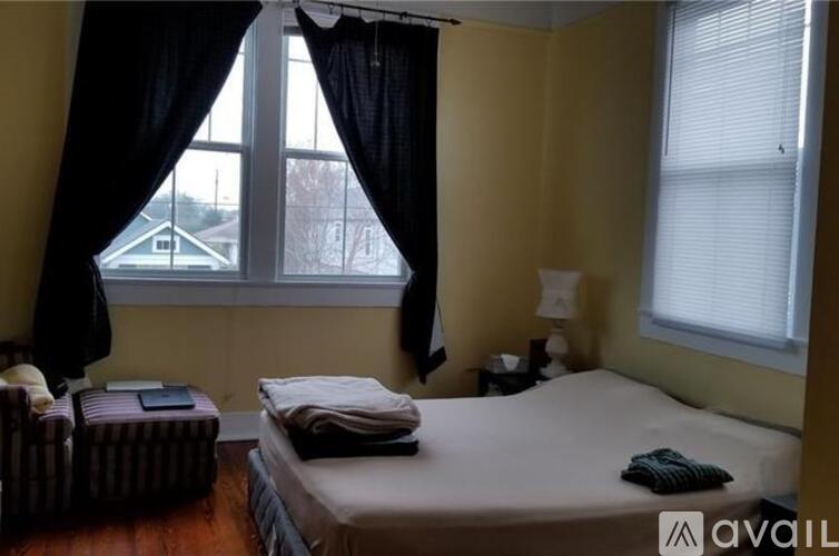 A bedroom with a bed, nightstand, and window with curtains.