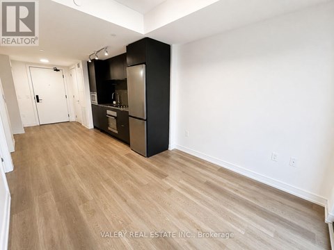 A kitchen area with a black refrigerator and wooden flooring.