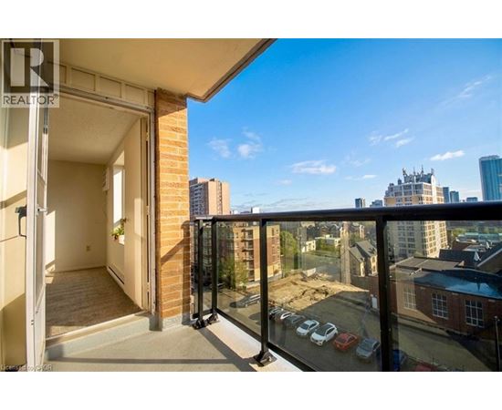 A balcony with a glass railing overlooks a parking lot and buildings.