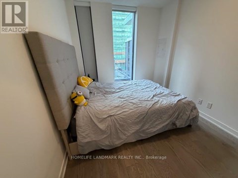 A bedroom with a bed covered in a grey comforter and a yellow stuffed animal on the headboard.