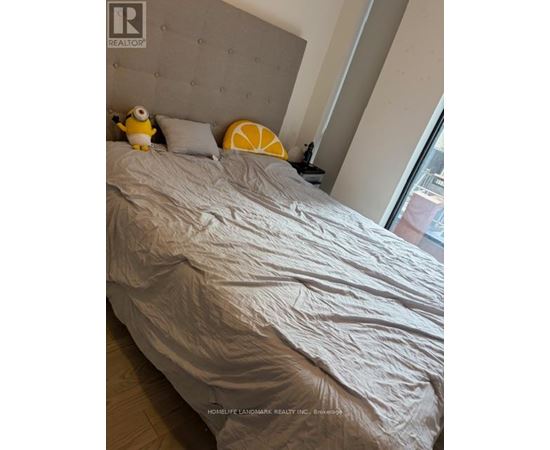 A bed with a grey headboard and a grey comforter with a yellow toy on it.
