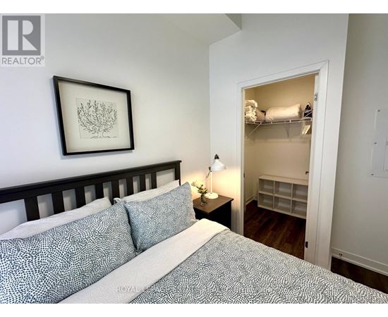 A bedroom with a bed, a nightstand with a lamp, and a framed picture on the wall.