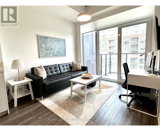 A living room with a black couch, a white desk, and a painting on the wall.