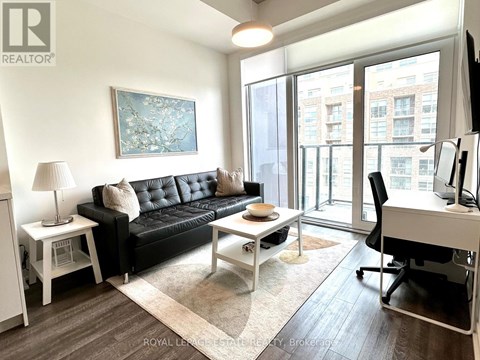 A living room with a black couch, a white desk, and a painting on the wall.