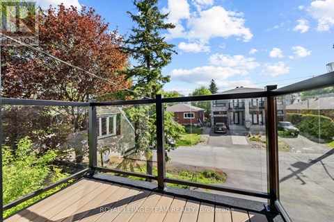 A balcony with a wooden floor and a glass railing overlooks a parking lot and buildings.