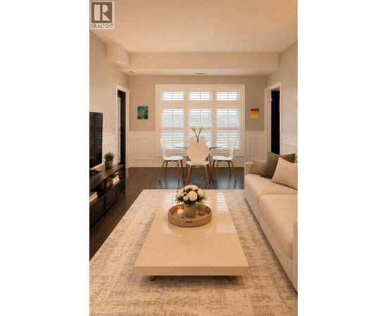 A living room with a white couch, a coffee table with a bowl of flowers, and a large window with blinds.