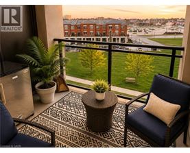 A balcony with a chair, table and potted plants overlooks a parking lot and buildings.