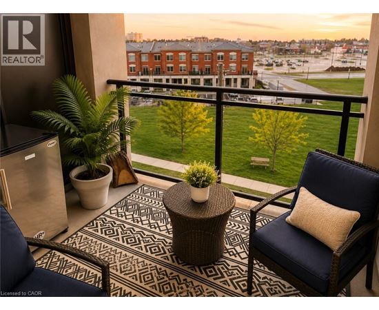 A balcony with a chair, table and potted plants overlooks a parking lot and buildings.