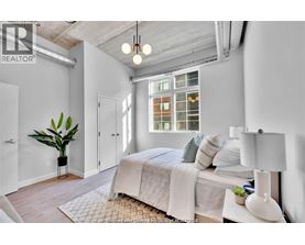 A bedroom with a bed, a potted plant, and a window with a view of a building.