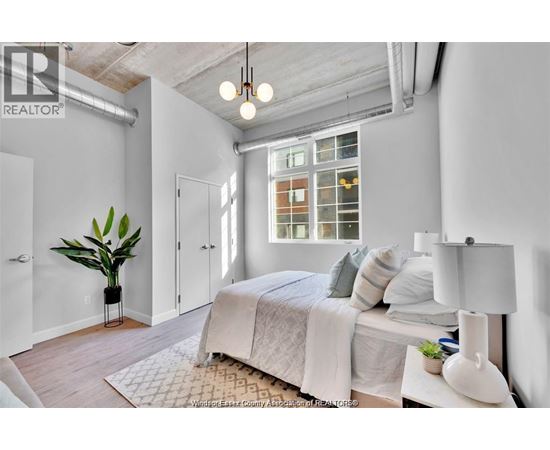 A bedroom with a bed, a potted plant, and a window with a view of a building.