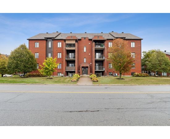 A red brick apartment building with a parking lot in front.