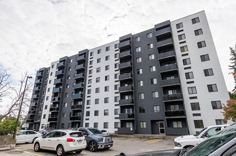 A large grey apartment building with cars parked in front.