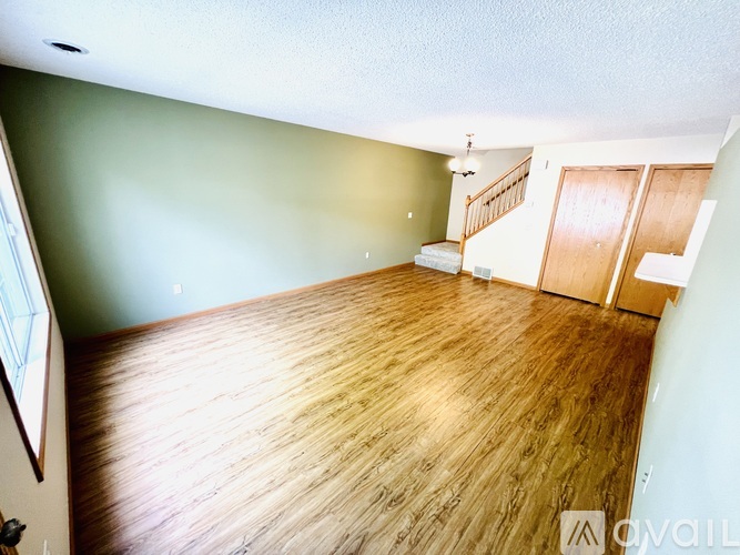 A room with wooden flooring and a staircase in the background.