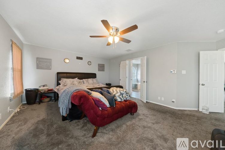 A bedroom with a bed, a red chair, and a ceiling fan.