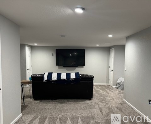 A living room with a black couch and a television mounted on the wall.