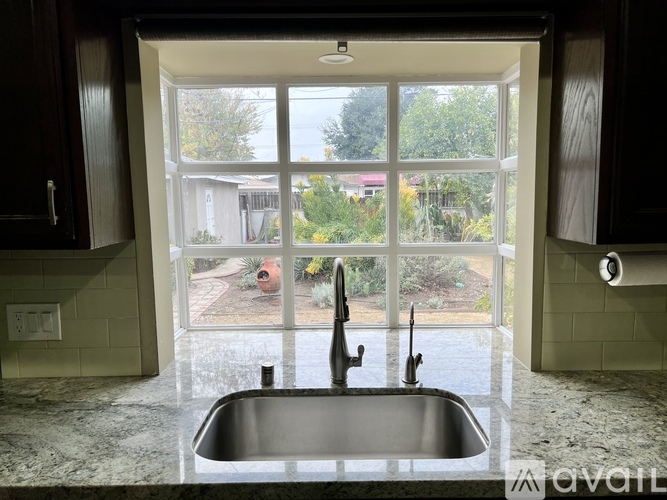 A kitchen with a sink and a window overlooking a backyard.