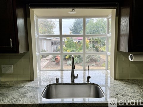 A kitchen with a sink and a window overlooking a backyard.