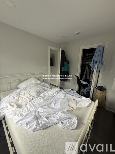 A bedroom with a messy bed and a closet with clothes hanging.