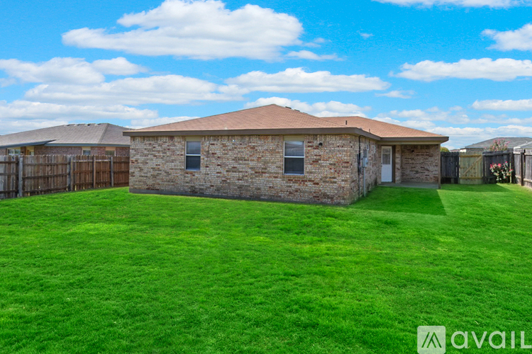 A house with a brown roof and a stone exterior is surrounded by a green lawn.