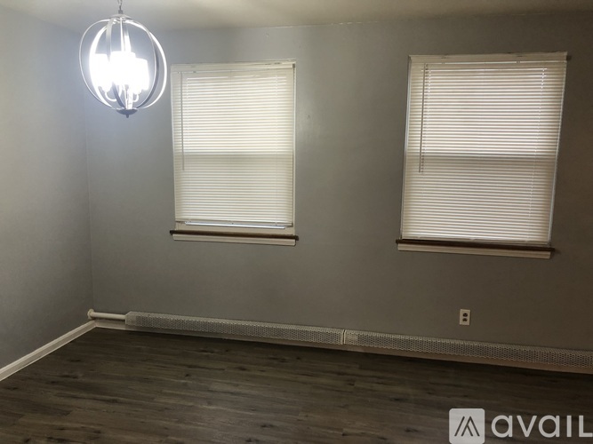 A room with a wooden floor and two windows with blinds.