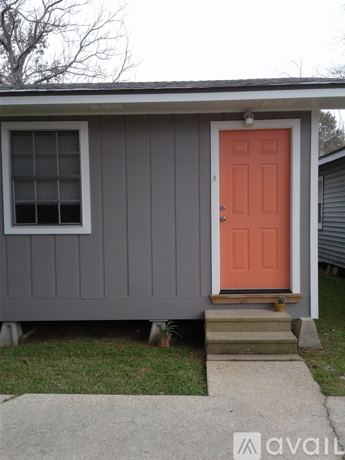 A small house with a grey exterior and a bright orange door.