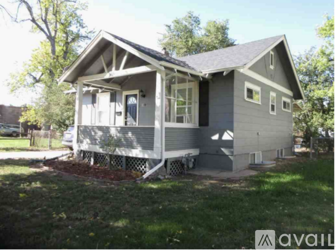 A small house with a porch is surrounded by grass and trees.