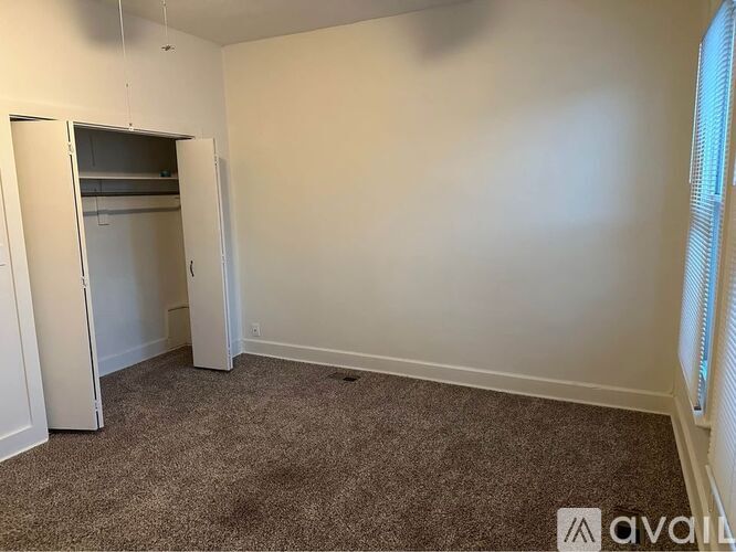 A carpeted room with a closet and a window.
