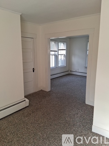 A room with a carpeted floor and a window with white curtains.