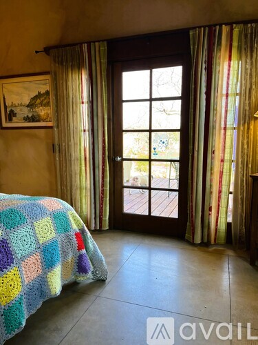 A bedroom with a bed covered in a multicolored blanket and a painting on the wall.
