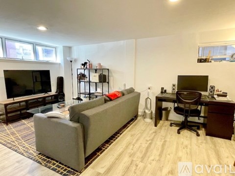 A living room with a grey couch, a television, and a desk with a chair.