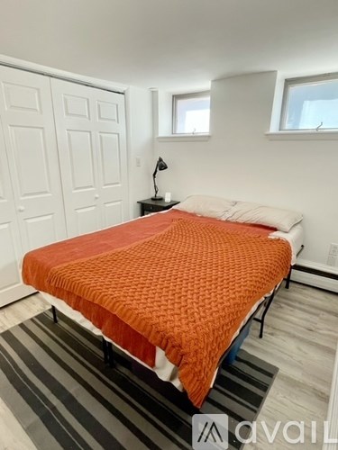 A bed with an orange blanket is in a room with white walls and a striped rug.