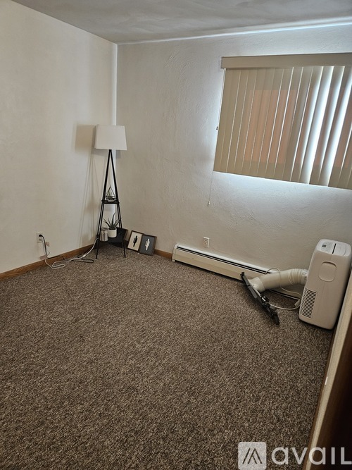 A room with a carpeted floor, a white lamp, a white wall, and a window with blinds.