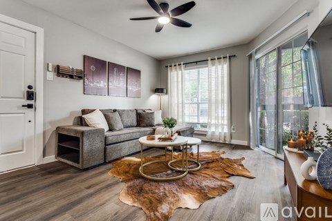 A living room with a grey couch, a brown cowhide rug, and a ceiling fan.