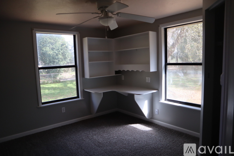 A room with a ceiling fan and a window overlooking a green area.