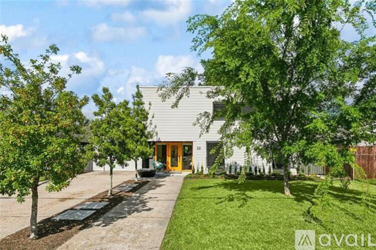 A house with a grey exterior and a yellow door is surrounded by green trees.