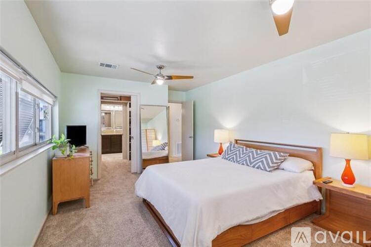 A bedroom with a large bed, a ceiling fan, and a nightstand with a lamp.