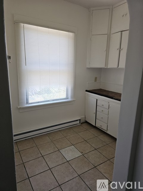 A kitchen with white cabinets and a window with blinds.