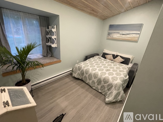 A bedroom with a bed, a plant, and a painting on the wall.