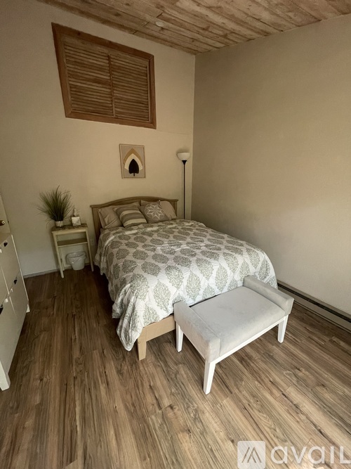 A bedroom with a bed, nightstand, and a wooden floor.