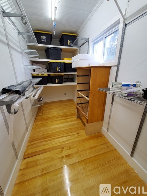 A room with wooden floors and white walls, containing a shelf, a cabinet, and some storage boxes.