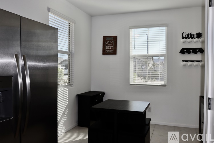 A kitchen with a fridge, a table and a window with blinds.