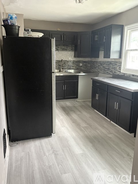 A black refrigerator stands in a kitchen with wooden floors and black cabinets.