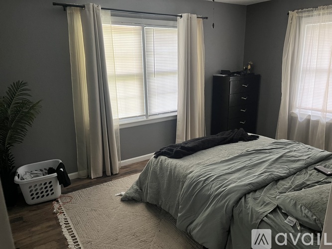 A bedroom with a bed, dresser, and window with curtains.