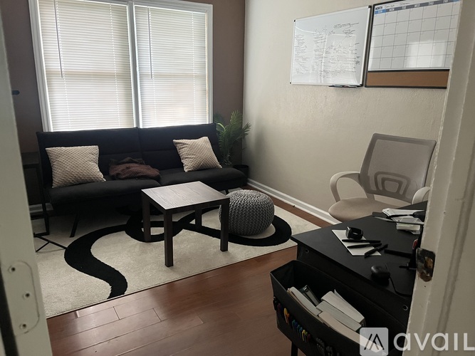 A black couch with two white pillows and a grey pouf on a black and white rug in a room.